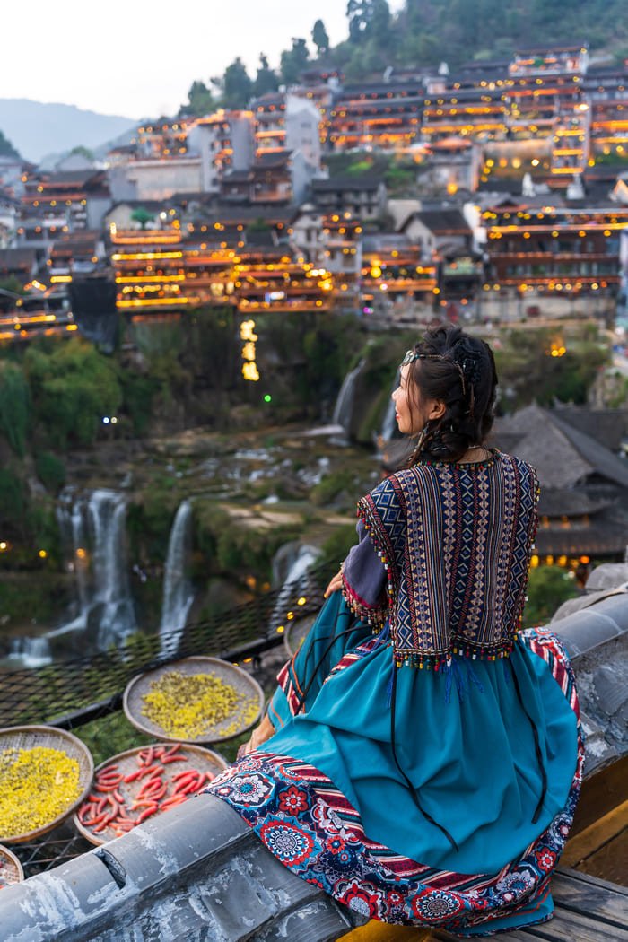 Mujer tradicional en tejado mirando ciudad antigua y cascadas iluminadas